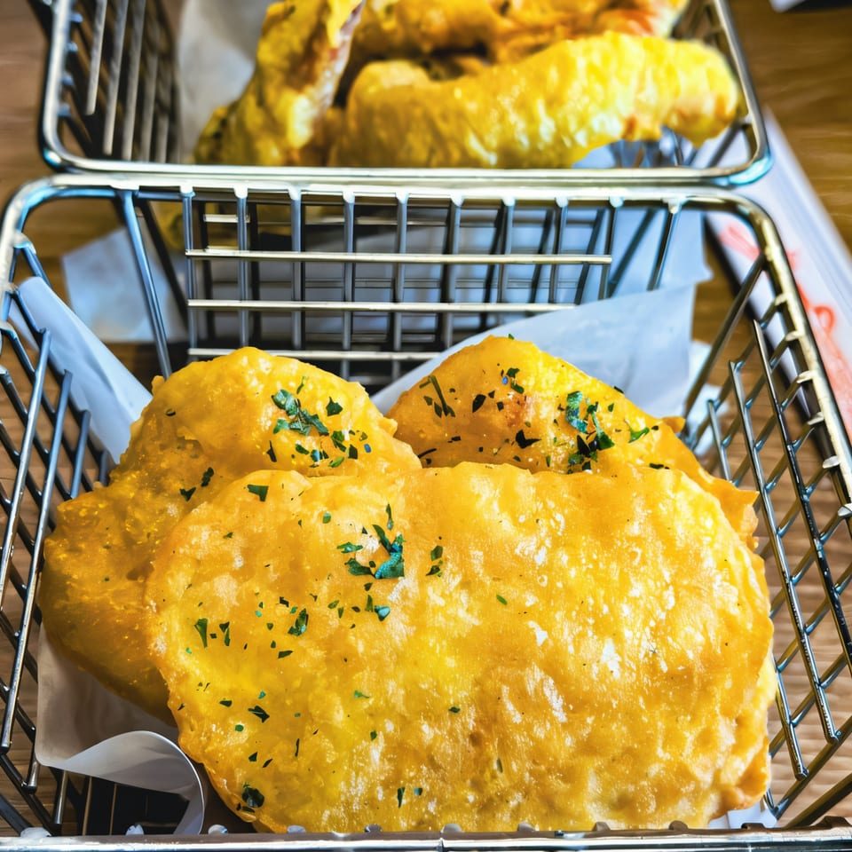 Golden-fried Korean dumplings, garnished with herbs, served in metal baskets on a wooden table.