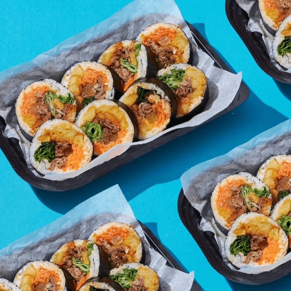 Multiple trays of Halgatteok Northridge's Korean gimbap rolls with various fillings on a blue surface.